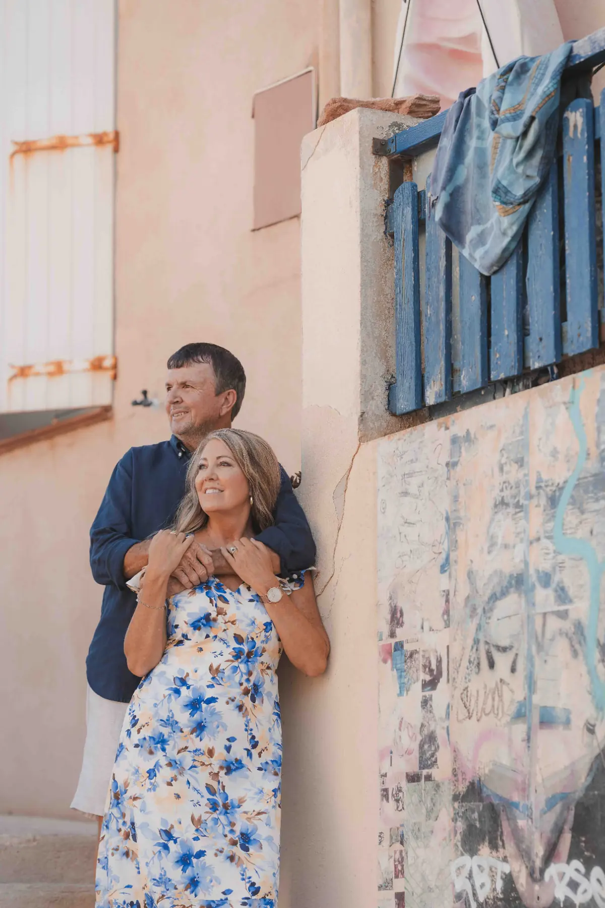 Couple embracing against a pastel facade with blue shutters in Malmousque, Marseille, in warm morning light