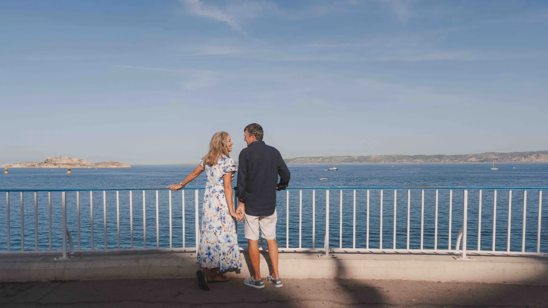 Couple looking at each other by the seafront railing facing the Frioul islands — photo walk on the Corniche, Marseille