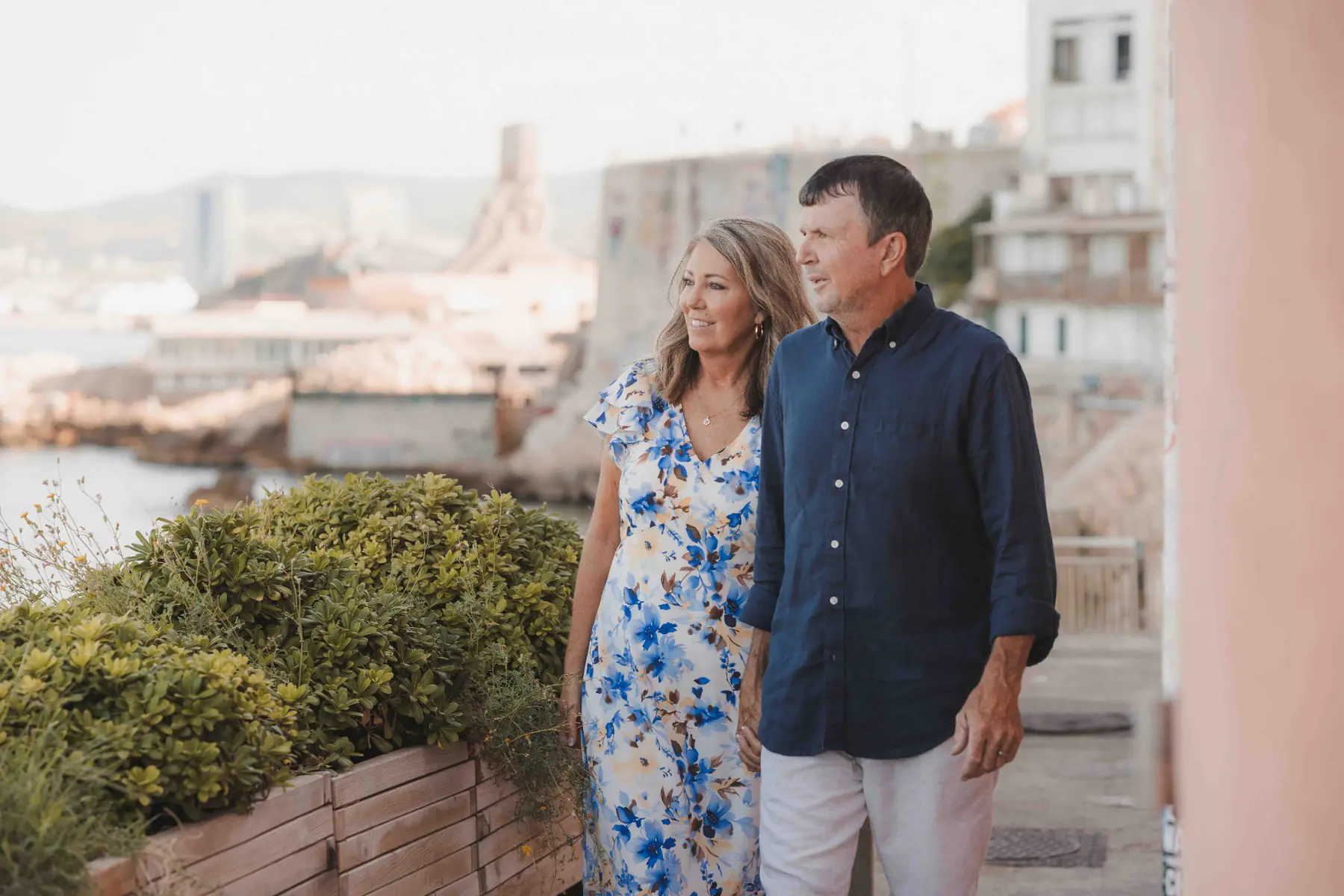 Couple walking along the Corniche with the sea and rooftops behind them — vacation photo session in Marseille